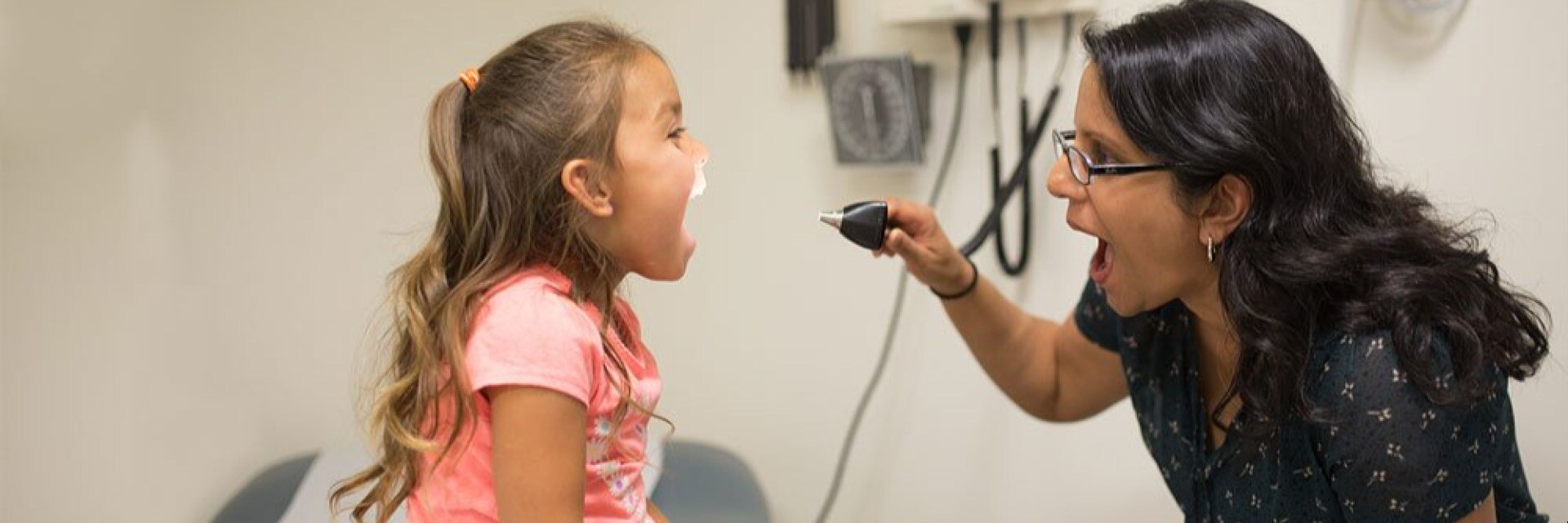 Provider looks into child patient's mouth with otoscope while child opens mouth and says "ah"